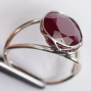 May include: A silver ring with a large, faceted, dark red gemstone set in a delicate silver frame.