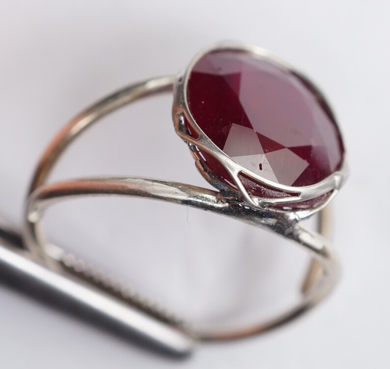 May include: A silver ring with a large, faceted, dark red gemstone set in a delicate silver frame.