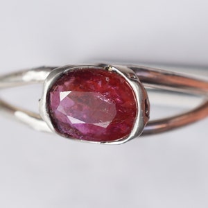 Puede incluir: Un anillo de plata con una piedra ovalada de color rojo oscuro engastada en un engaste de bisel.