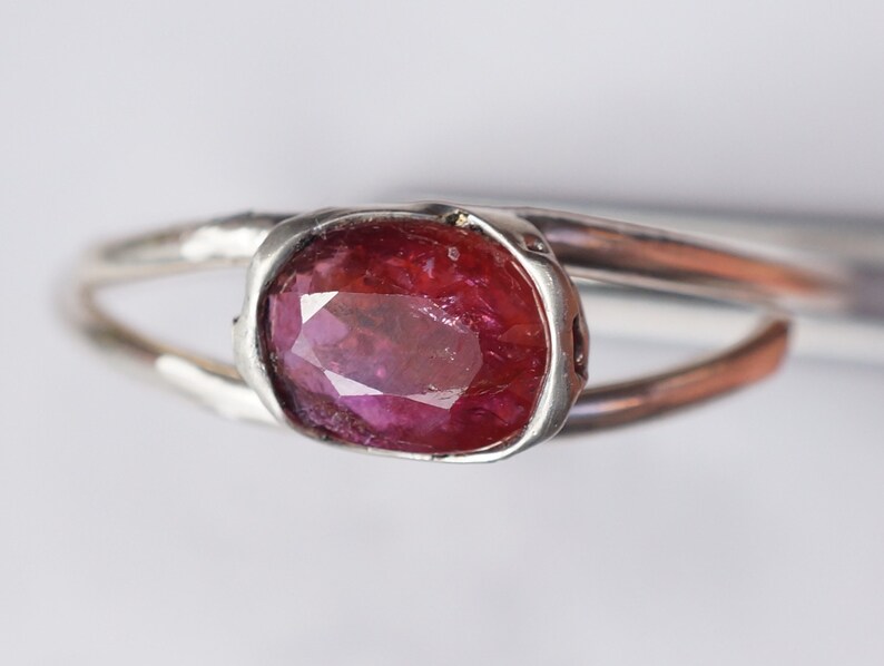 Puede incluir: Un anillo de plata con una piedra ovalada de color rojo oscuro engastada en un engaste de bisel.