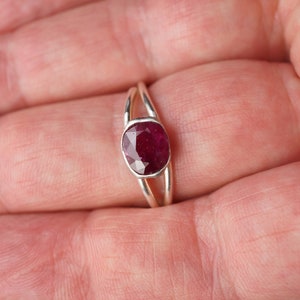 Op de afbeelding: Een zilveren ring met een dieprode robijn-edelsteen gezet in een bezel-setting. De ring heeft een delicate, gedraaide band.