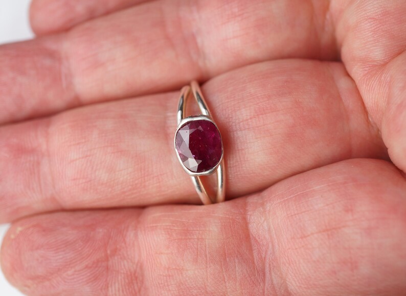 Op de afbeelding: Een zilveren ring met een dieprode robijn-edelsteen gezet in een bezel-setting. De ring heeft een delicate, gedraaide band.