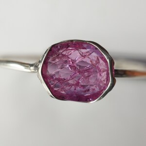 May include: A silver ring with a large, pink, faceted gemstone. The gemstone is set in a bezel setting and has a rough, natural look.