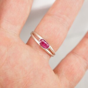 May include: A silver ring with a delicate double band design features a vibrant pink oval-shaped gemstone.