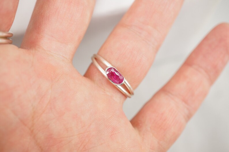 May include: A silver ring with a delicate double band design features a vibrant pink oval-shaped gemstone.