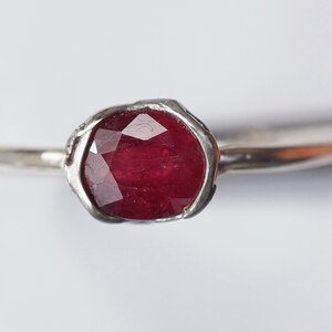 Pode incluir: Um anel de prata com uma gema de rubi vermelho engastada em uma banda texturizada.