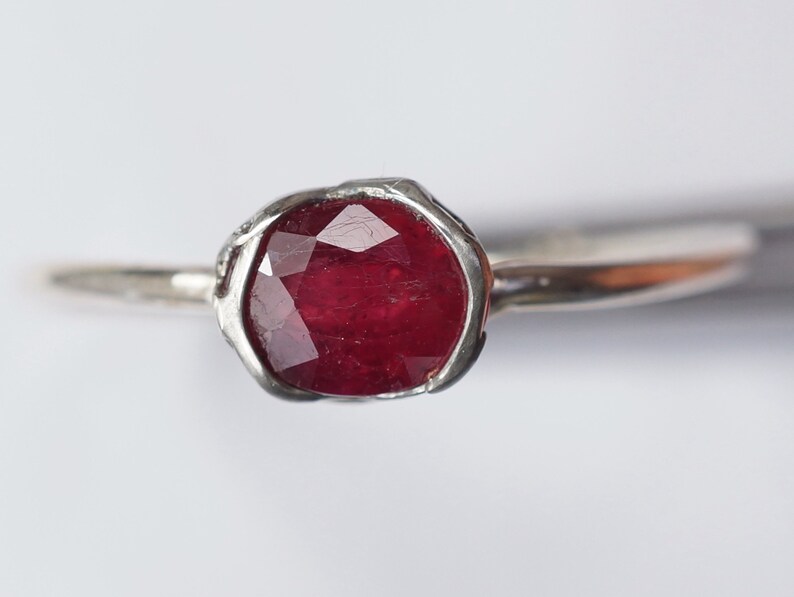 Pode incluir: Um anel de prata com uma gema de rubi vermelho engastada em uma banda texturizada.