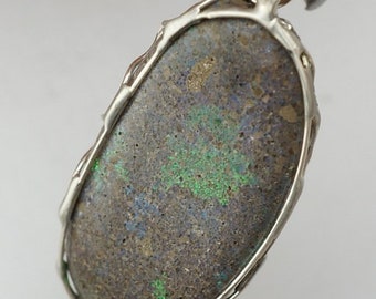 May include: A silver pendant with a dark gray oval opal stone set in a silver wire frame. The opal has green and blue iridescent flashes.