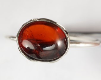 Könnte beinhalten: Ein silberner Ring mit einem großen, ovalen, dunkelroten Edelstein.