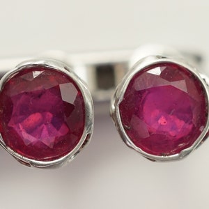 May include: A pair of silver earrings with a round, faceted, pink gemstone in each earring.