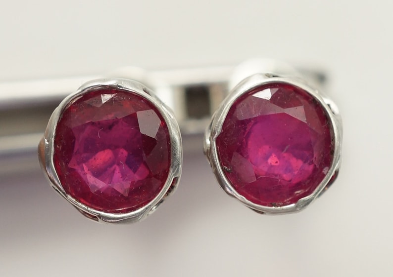May include: A pair of silver earrings with a round, faceted, pink gemstone in each earring.