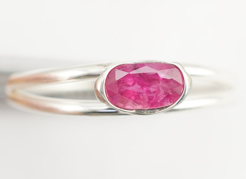 May include: A silver ring with a pink oval-shaped gemstone set in a bezel setting.