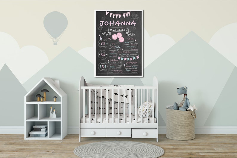 Puede incluir: Una cuna blanca con una s&aacute;bana con estampado de flechas blancas y negras. A la izquierda de la imagen hay una estanter&iacute;a blanca con forma de casa. Un letrero de pizarra con el texto "Johanna Mein 1. Geburtstag" est&aacute; colgado en la pared. Un animal de peluche gris est&aacute; sentado en una cesta beige.