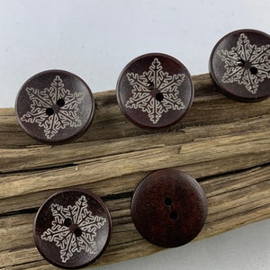 Könnte beinhalten: Fünf braune Holz-Knöpfe mit Schneeflocken-Design. Die Schneeflocken sind weiß und die Knöpfe haben zwei Löcher.