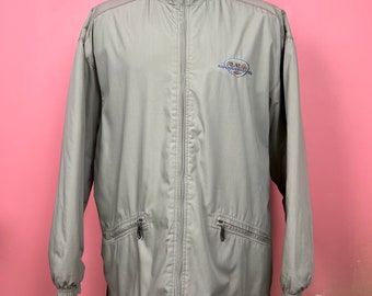 May include: A tan zip-up jacket with a blue fleece-lined collar. The jacket has two zippered pockets and a small logo on the chest. The jacket is displayed on a mannequin against a pink background.