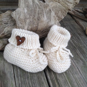May include: A pair of white knitted baby booties with a wooden heart button on one bootie.