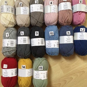 May include: A collection of 15 balls of yarn in various colors, including white, beige, gray, pink, red, yellow, and green. Each ball is labeled with a number from 1 to 15.