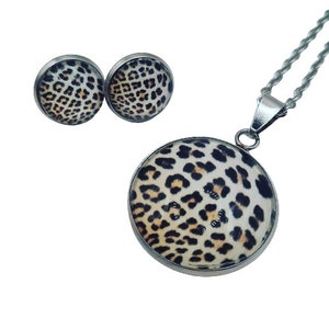Può includere: Un set di gioielli composto da una collana e orecchini con un design a stampa leopardata. La collana ha un ciondolo rotondo con una catena d'argento. Gli orecchini sono piccoli e rotondi con perni d'argento.
