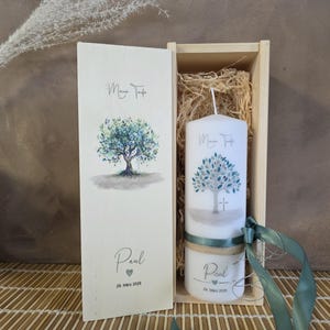 Könnte beinhalten: Ein Taufkerzen- und Andenken-Box-Set. Die weiße Kerze und die Box zeigen ein Aquarell-Baumdesign mit dem Text "Meine Taufe" und "Paul". Das Set enthält ein kleines Glas mit passendem Design und einem grünen Band.