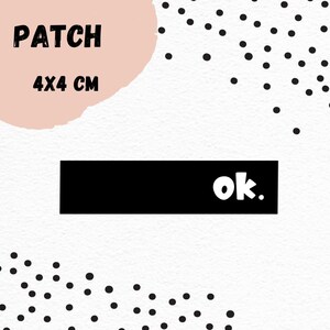 Könnte beinhalten: Schwarz-weißes Bügelbild mit dem Wort "ok." in weißer Schrift. Das Bügelbild ist 4x4 cm groß und befindet sich auf einem weißen Hintergrund mit schwarzen Punkten.