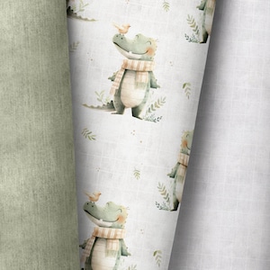 Könnte beinhalten: Ein weißer Hintergrund mit einem sich wiederholenden Muster aus grünen Alligatoren, die einen braunen und weißen Schal tragen. Jeder Alligator hat einen kleinen gelben Vogel auf dem Kopf. Der Hintergrund hat ein subtiles grünes und weißes Gittermuster.