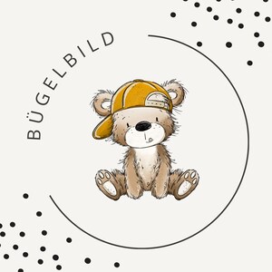 May include: A brown teddy bear illustration wearing a yellow baseball cap, positioned inside a thin black circular frame. The text BÜGELBILD is printed in black to the left of the bear, and black polka dots are scattered in the corners.