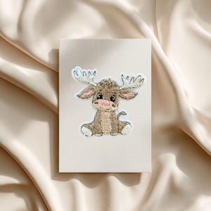 Può includere: Una toppa ricamata a forma di alce su una carta beige chiaro. L'alce ha grandi corna, un corpo marrone e dettagli bianchi. Ideale per abbigliamento o progetti artigianali.