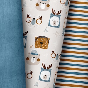 Könnte beinhalten: Ein weißer Stoff mit einem sich wiederholenden Muster aus verschiedenen Tiergesichtern. Zu den Tieren gehören Bären, Hirsche und ein Fuchs. Der Stoff ist von zwei anderen Stoffen umgeben, einem blauen und einem mit braunen und blauen Streifen.