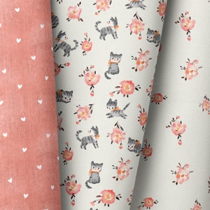 Könnte beinhalten: Ein weißer Stoff mit einem sich wiederholenden Muster aus grauen Kätzchen und rosa Blumen. Der Stoff ist über einen rosa Stoff mit weißen Punkten gefaltet.