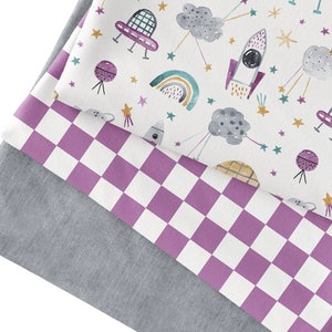 May include: Three fabric swatches, one with a white background and a repeating pattern of rockets, clouds, rainbows, and stars, one with a white background and a purple and white checkered pattern, and one with a solid gray background.