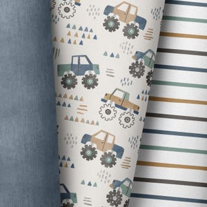 May include: A white fabric with a repeating pattern of blue and brown monster trucks with large wheels. The background has a pattern of small blue, green, and brown triangles, dots, and lines.