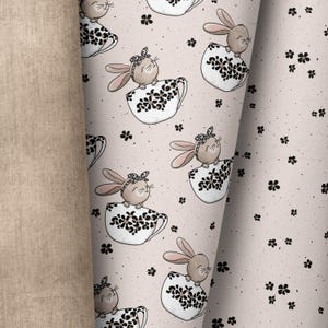 Puede incluir: Una tela rosa con un patrón repetido de conejos marrones sentados en tazas de té con un diseño de estampado de leopardo. Las tazas de té tienen acentos florales negros. El fondo es rosa claro con flores negras dispersas.
