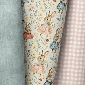 May include: A white fabric with a repeating pattern of brown bunnies wearing pink and blue dresses. The bunnies are surrounded by small yellow and pink flowers. The fabric is next to a pink and white gingham fabric.