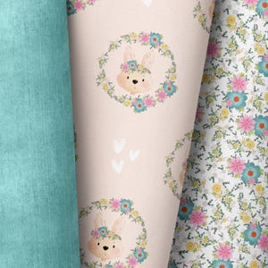Può includere: Un tessuto rosa e bianco con un motivo ripetitivo di coniglietti che indossano corone di fiori. I coniglietti sono circondati da piccoli fiori e foglie. Il tessuto è perfetto per progetti di artigianato, come la creazione di trapunte, cuscini o borse.