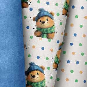Può includere: Tessuto bianco con un motivo ripetuto di un orso marrone che indossa un cappello blu e una sciarpa verde. L'orso è circondato da pois verdi, blu e arancioni.