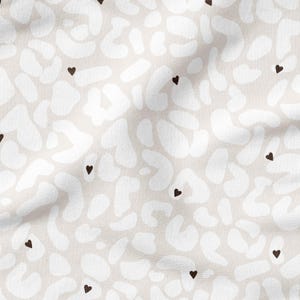 Puede incluir: Una tela beige con un patrón abstracto blanco y corazones negros dispersos.