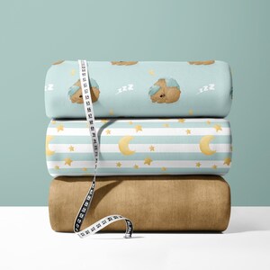 May include: Three rolls of fabric with a blue and white striped pattern, a blue pattern with sleeping bears and stars, and a brown fabric. A white measuring tape is wrapped around the rolls of fabric.