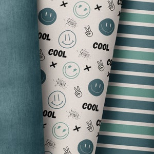 May include: A white fabric with a repeating pattern of blue smiley faces, peace signs, and the word "COOL". The fabric is folded over a blue striped fabric.