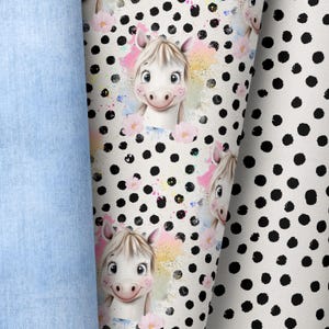 Könnte beinhalten: Weißer Stoff mit schwarzem Punkte-Muster. Der Stoff zeigt ein sich wiederholendes Design eines Cartoon-Pferdes mit rosa Blumen und bunten Aquarell-Spritzen.