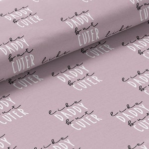 May include: A pink fabric with a repeating pattern of the text "like daddy but cuter" in black and white.