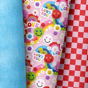 Puede incluir: Tela estampada rosa y blanca con un diseño repetitivo de arcoíris, caras sonrientes, flores y el texto "Love You" y "Love & Pride".