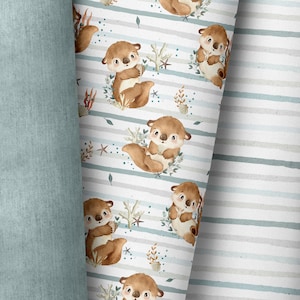 Könnte beinhalten: Ein weißer Stoff mit einem sich wiederholenden Muster aus braunen Ottern, die Muscheln halten, umgeben von grünem Seetang und blauen und weißen Streifen. Der Stoff hat einen hellblauen Hintergrund mit weißen und grauen Streifen.