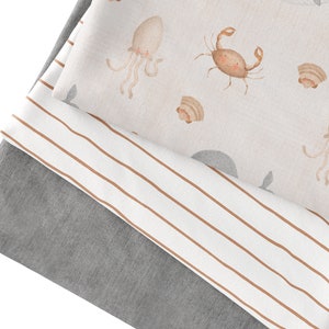 May include: Three fabric swatches, one with a light brown and white striped pattern, one with a light gray solid color, and one with a light pink background with a repeating pattern of brown sea creatures, including crabs, octopuses, and seashells.