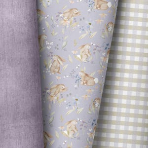 Può includere: Un tessuto viola con un motivo di coniglietti bianchi e fiori. Il tessuto è accanto a un tessuto gingham bianco e marrone chiaro.