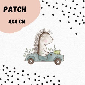 Könnte beinhalten: Ein 4x4 cm großer Aufnäher mit einer Illustration eines Igels, der ein hellblaues Auto fährt, mit einem grünen Frosch. Das Wort "PATCH" steht in fetter schwarzer Schrift.