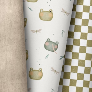 May include: A white background with a repeating pattern of green frogs and dragonflies. The frogs have different expressions and some have a pink belly. The dragonflies are a light pink colour.
