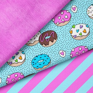 Op de afbeelding: Een close-up van drie verschillende stoffen. Eén is effen magenta van kleur, een andere is lichtblauw met een patroon van donuts met hartjes-sprinkles, en de derde is lichtblauw met magenta strepen. De donuts hebben witte, roze en bruine glazuur.