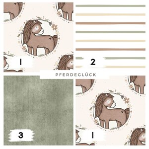 Può includere: Campioni di tessuto con disegni equestri. Uno presenta un motivo ripetuto di un cavallo marrone all'interno di una ghirlanda floreale. Un altro mostra strisce orizzontali in tonalità neutre. Il terzo è verde unito. Il testo "PFERDEGLÜCK" è visibile.