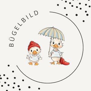 Op de afbeelding: Illustratie van twee cartoon eenden. Eén eend draagt een rode muts en de andere houdt een gestreepte paraplu vast. Beide eenden dragen gestreepte shirts. Het woord "BÜGELBILD" is in een cirkel rond de eenden geschreven.