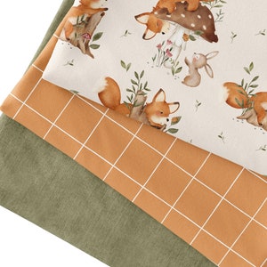 Può includere: Tre campioni di tessuto: un tessuto verde con una texture sottile, un tessuto arancione con un motivo a griglia bianca e un tessuto bianco con un motivo ripetitivo di volpi, conigli e funghi.